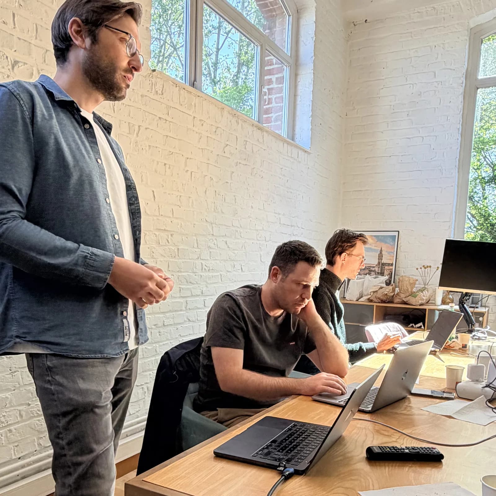 Un expert Hoko debout accompagne deux développeurs au travail sur leurs ordinateurs.