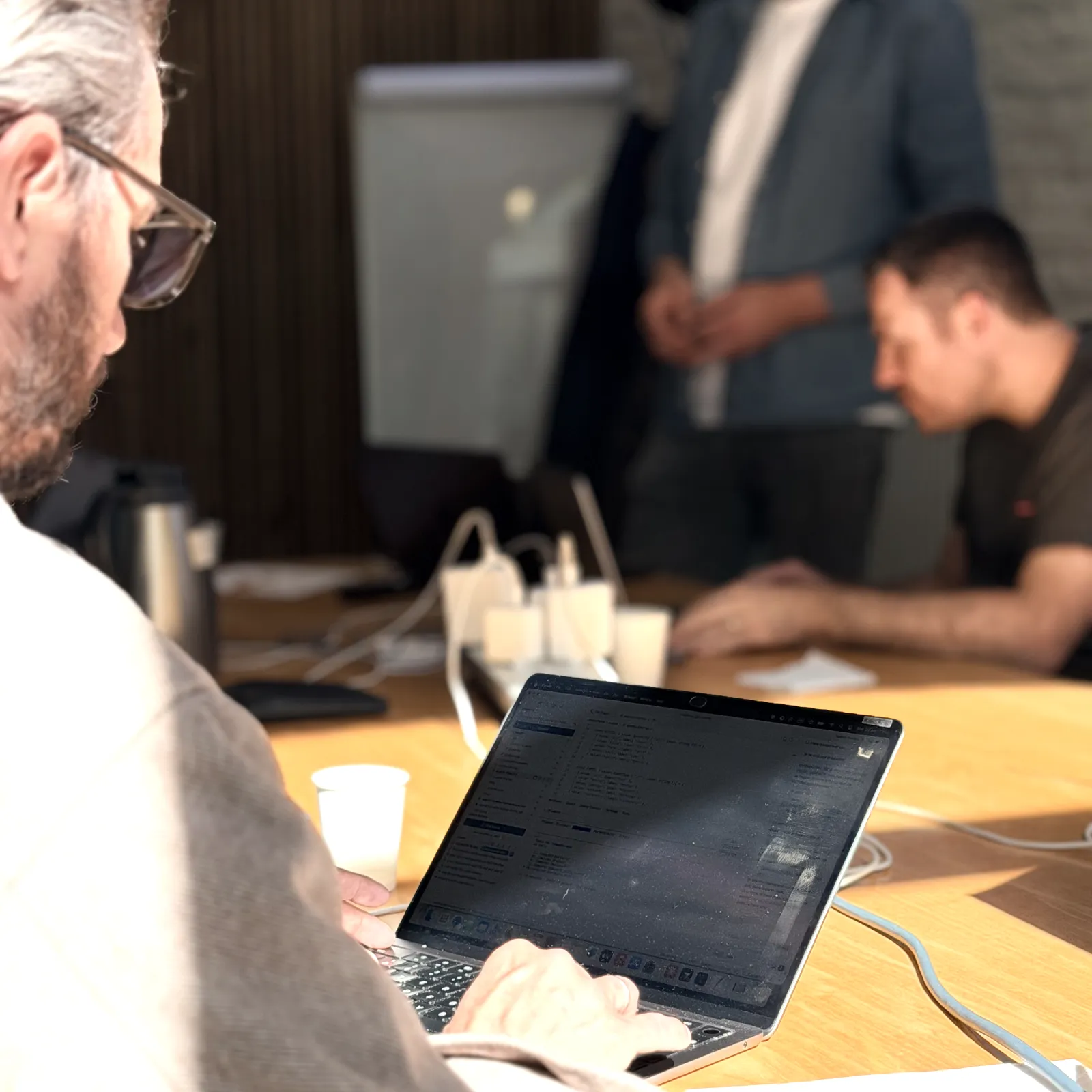 Atelier Hoko : un participant travaille sur son ordinateur portable, un formateur accompagne un développeur à l'arrière-plan.