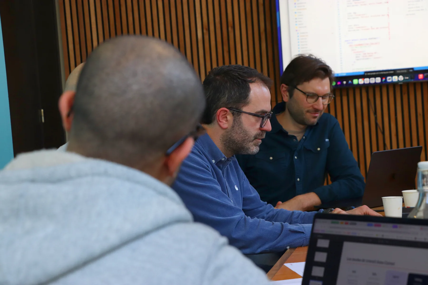 Atelier Hoko : des développeurs travaillent sur leurs portables devant un écran de code.