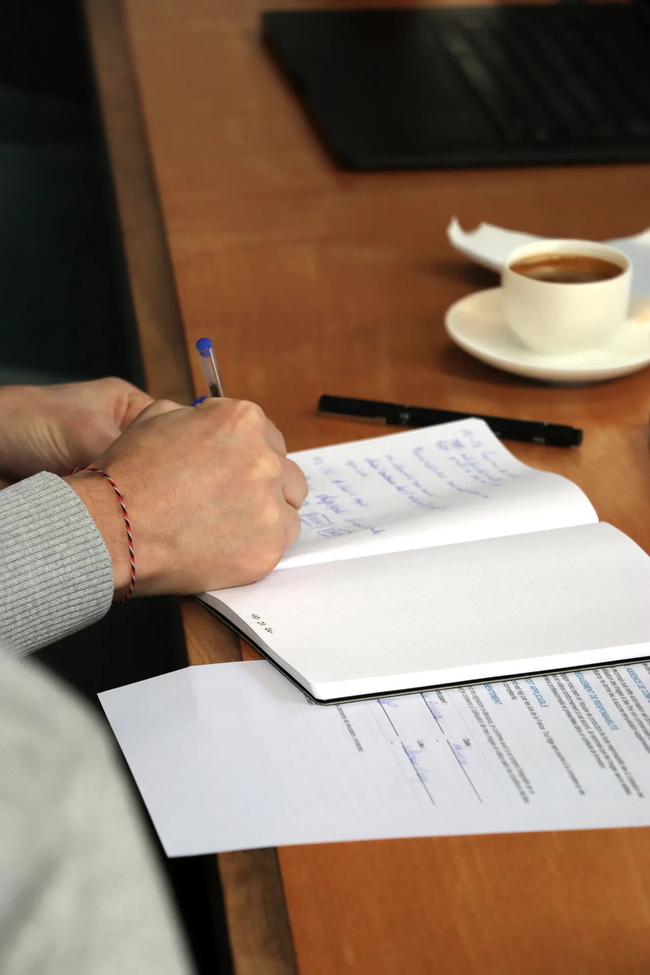 Prise de notes manuscrite dans un carnet pendant un atelier Hoko, une tasse de café sur la table.